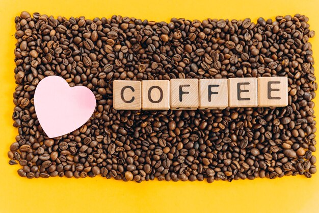 Słowo kawa napisane na drewnianych kostkach i ziarnach kawy na żółtym tle