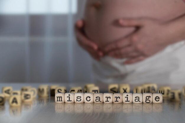 Zdjęcie słowo miscarriage złożone z drewnianych liter. kobieta w ciąży w tle