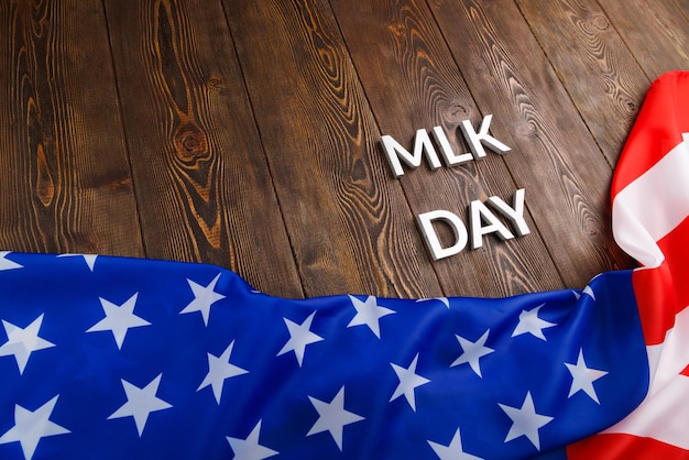 Słowo mlk day nałożone srebrnymi metalowymi literami na drewnianej powierzchni z pogniecioną flagą USA pod spodem