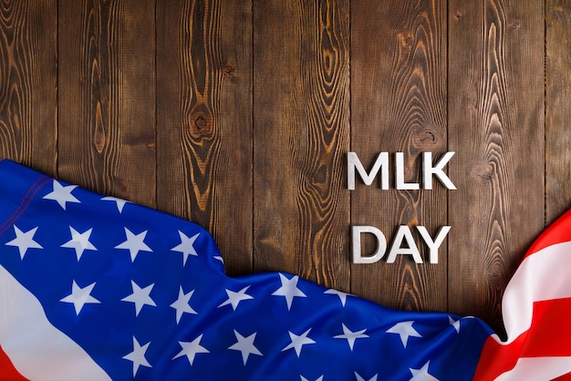 Słowo „MLK day” ułożone srebrnymi metalowymi literami na drewnianej powierzchni z pogniecioną flagą USA u dołu