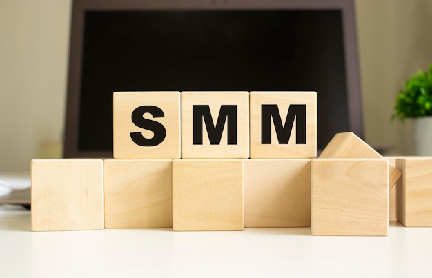 Słowo SMM jest napisane na drewnianych kostkach leżących na biurowym stole przed laptopem