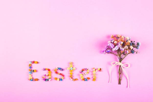 Słowo Wielkanoc napisane jest małymi kolorowymi kwiatami na fioletowym stole.
