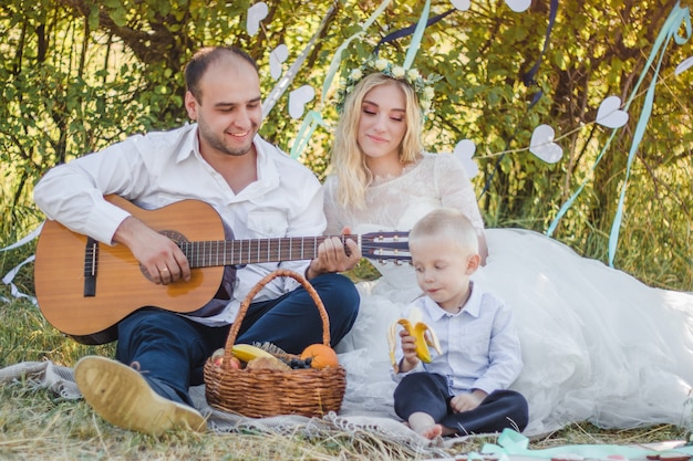 Ślub Na świeżym Powietrzu W Stylu Piknikowym Pan Młody Gra Na Gitarze Młoda Atrakcyjna Panna Młoda I Mały Chłopiec