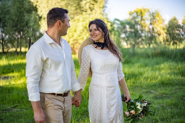 Ślub na zamku Stylowa i piękna suknia Księżniczki Bujna biała suknia i welon Panna młoda jest brunetką Pan młody w czarnym garniturze Para spaceruje po parku na terenie zamku