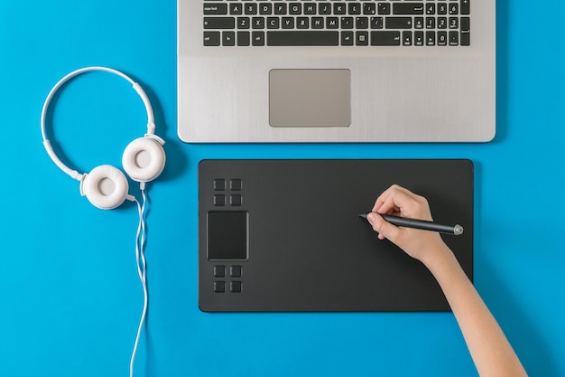Słuchawki do laptopa i ręka z tabletem graficznym na niebieskim tle Urządzenie do pracy w edytorach graficznych