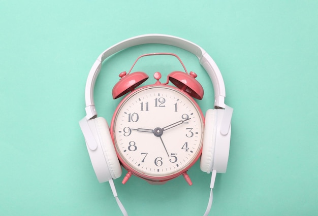 Słuchawki stereo z różowym budzikiem na niebieskim tle Minimalizm koncepcja muzyki Kreatywny układ Świeży pomysł