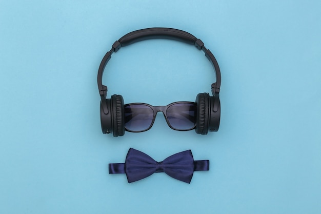Słuchawki z okularami przeciwsłonecznymi i muszką na niebieskim tle. Widok z góry