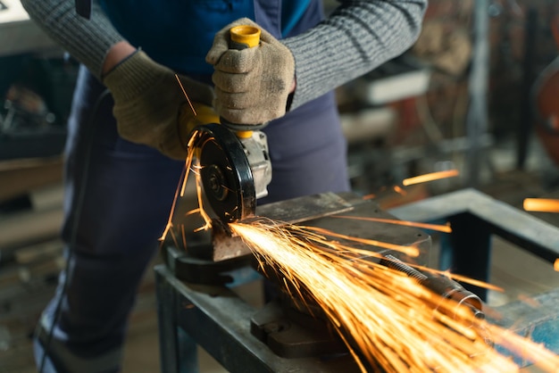 Ślusarz w odzieży specjalnej i goglach pracuje przy produkcji obróbki metalu szlifierką kątową