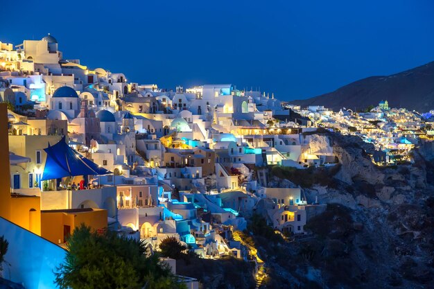 Słynna wioska Oia z białymi domami i niebieskimi kopułowymi kościołami podczas zachodu słońca na wyspie Santorini Morze Egejskie Grecja