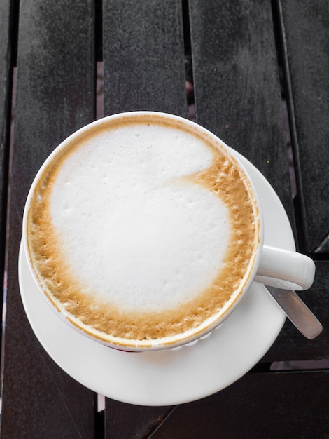 Smaczna biała filiżanka cappuccino z latte art na drewnianym stole