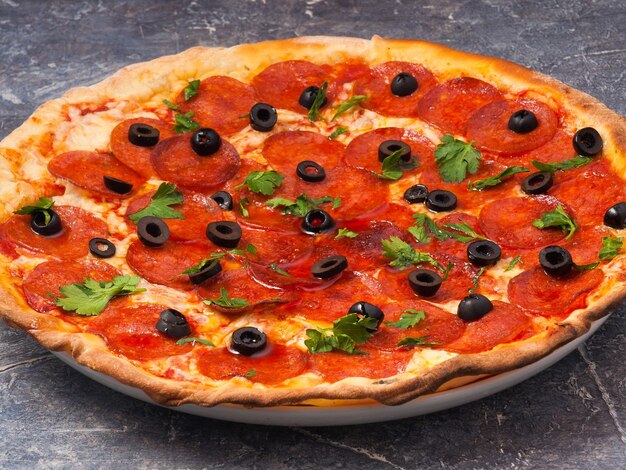 Smaczna pizza pepperoni z oliwkami i mozzarellą ozdobiona zieleniną