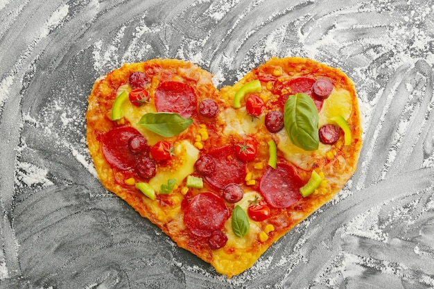 Smaczna pizza w kształcie serca na sproszkowanym stole z czarnej mąki