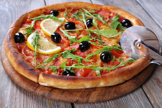 Smaczna pizza z ziołami i okrągłym nożem na pokładzie i drewnianym stole