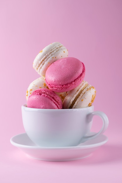 Zdjęcie smaczne francuskie macarons w różowo-białych kolorach i różnych smakach w białej filiżance