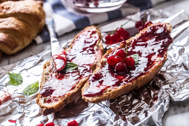 Smaczne śniadanie z marmoladą z czerwonej porzeczki croissanty masło i listkami mięty.