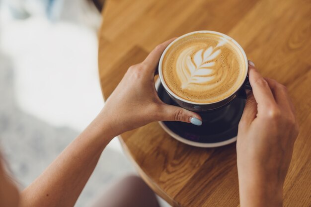 Smaczne świeże Cappuccino W Filiżance Na Drewnianym Stole. Nie Do Poznania Kobieta Trzyma Kubek W Ręce.