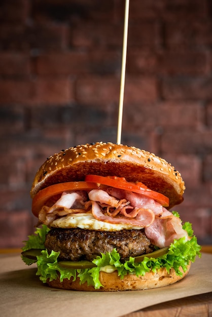Smaczny amerykański burger z wołowiną bekon i jajkiem na drewnianym stole ceglanym murem tło lato