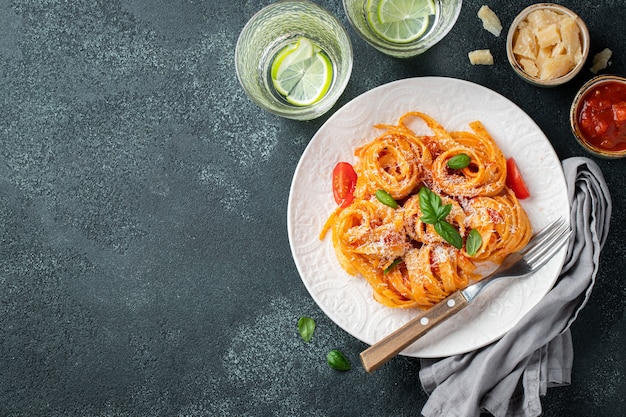 Smaczny apetyczny klasyczny włoski makaron tagliatelle z sosem pomidorowym, serem parmezanem i bazylią na talerzu na ciemnym stole. Widok z góry, poziomy. Widok z góry z miejscem na kopię