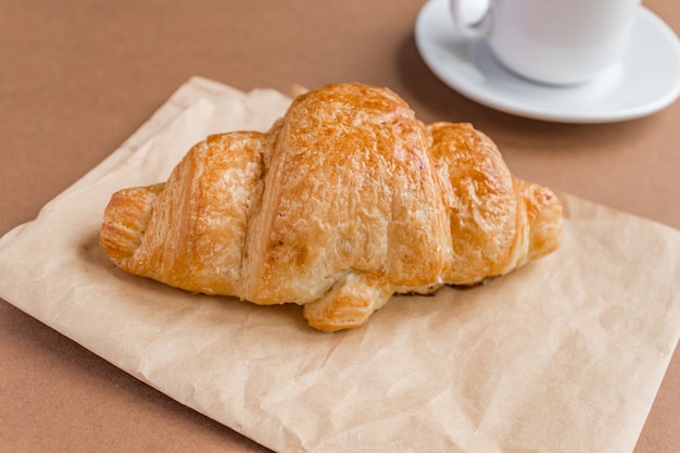 Smaczny breackfast. Francuski rogalik serwowany na białym talerzu i filiżance czarnej kawy lub espresso na brązowym tle. Skopiuj miejsce