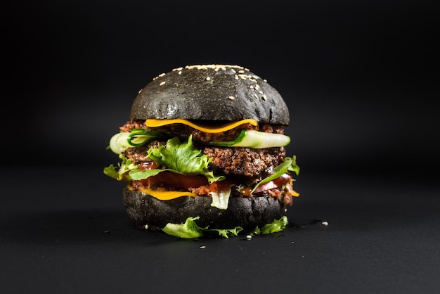 Zdjęcie smaczny burger rzemieślniczy z czarną bułką na czarnym tle