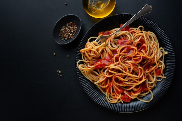 Smaczny klasyczny włoski makaron z sosem pomidorowym i serem na talerzu na ciemnym tle. Widok z góry.