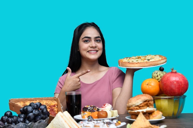 smakosz dziewczyna siedząca przy stole z owocami uśmiechnięta i trzymająca pizzę model indyjski pakistański