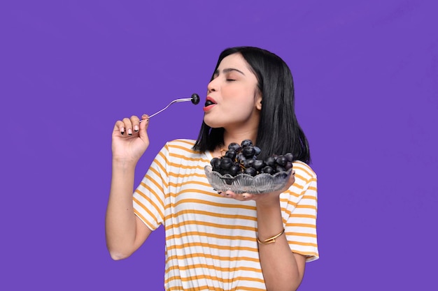 smakosz dziewczyna trzyma miskę winogron i winogron jej usta tło indyjski pakistański model