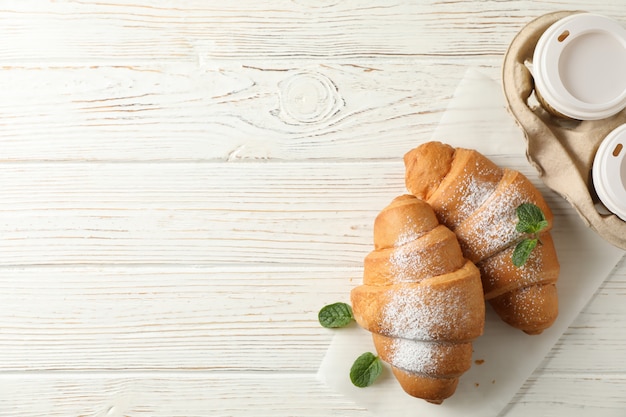 Smakowici croissants i filiżanki z kawą na drewnianym tle, odgórny widok