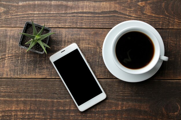Smartfon biały i filiżankę kawy na brązowym drewnianym stole. widok z góry