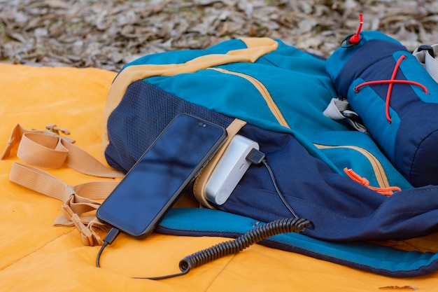 Smartfon jest ładowany za pomocą przenośnej ładowarki. Power bank z telefonem komórkowym na śpiworze z plecakiem.