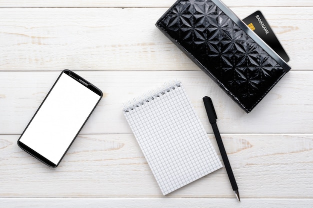 Smartfon, notatnik, długopis i karta kredytowa na białym stole