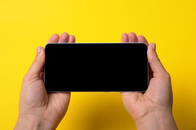 Smartfon w kobiecych rękach z czarnym ekranem na żółtym tle