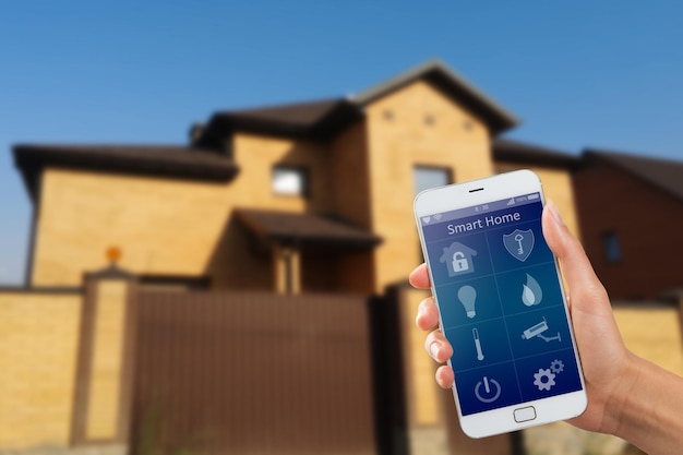 Smartfon z aplikacją ochrony domu w dłoni na tle budynku