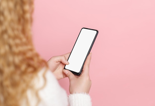 Smartfon z białym pustym ekranem w rękach kobiety na różowym tle