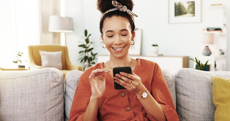 Zdjęcie smartphone gry i kobieta w domu kanapa i chłodzenie w salonie uśmiech i odpoczynek w mieszkaniu lounge spokój i szczęśliwy w weekend mobilny i wygodny na kanapie gra i wygrać w domu