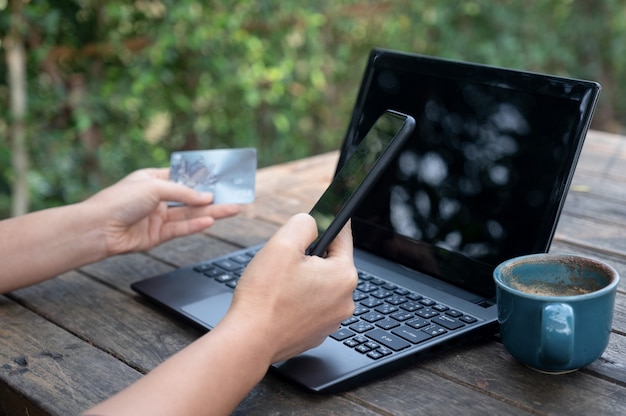 Smartphone i kredytowe karty w ręce z laptopem i kawą na drewnianym stole.