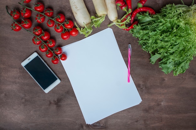 Smartphone na stole w kuchni na tle świeżych warzyw. Tło żywności Miejsce na tekst. Tabela menu w tle. Zdrowa równowaga żywności.