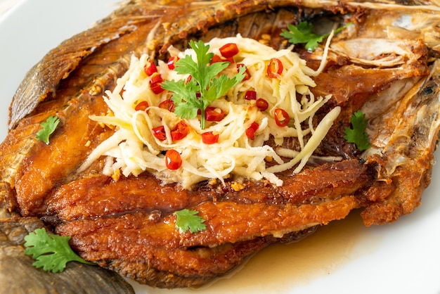 Smażona ryba okonia morskiego z sosem rybnym i pikantną sałatką na talerzu