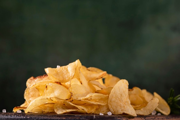 Smażone chipsy ziemniaczane z solą morską, na drewnianej desce, zbliżenie