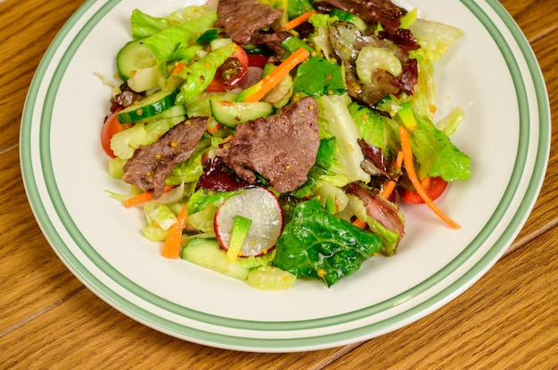 Smażone mięso z warzywami. Sałatka z mięsem, pomidorami, papryką, ogórkami i surówką na podłoże drewniane