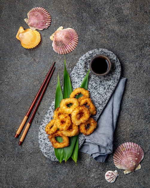 Zdjęcie smażone pierścienie kałamarnic na kamiennej płytce ozdobione tropikalnymi liśćmi azjatycka koncepcja jedzenia sos sojowy i pałeczki