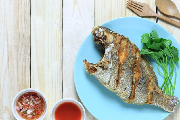 Smażone ryby morskie w naczyniu na drewnianej podłodze i tajskim sosie przyprawowym.