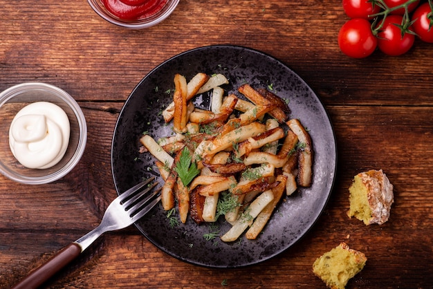 Smażone Ziemniaki Na Talerzu Z Ziołami Na Drewnianym Tle. Ketchup, Majonez I Chleb Leżą Obok Siebie.