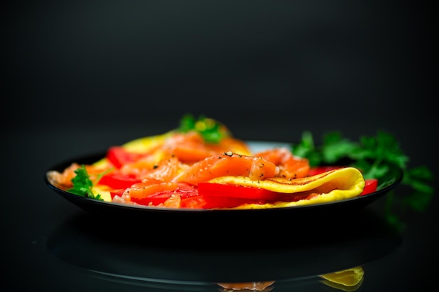 Smażony omlet z pomidorami, warzywami i kawałkami lekko solonej czerwonej ryby wyizolowanej na czarnym tle