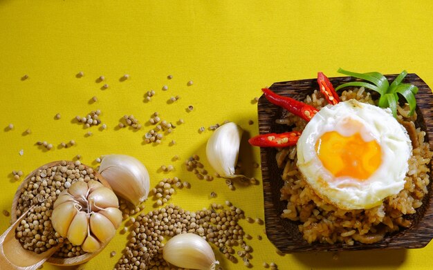 Smażony ryż ozdobiony jajkiem, chili, czosnkiem i kolendrą na drewnianym talerzu na żółtym tle