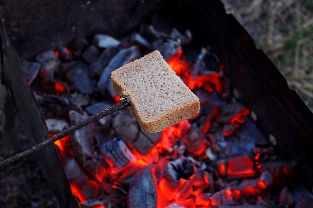 Zdjęcie smażyć chleb na ognisku na biwaku, chleb nadziewany na kij nad węglami, gotować razowe pieczywo