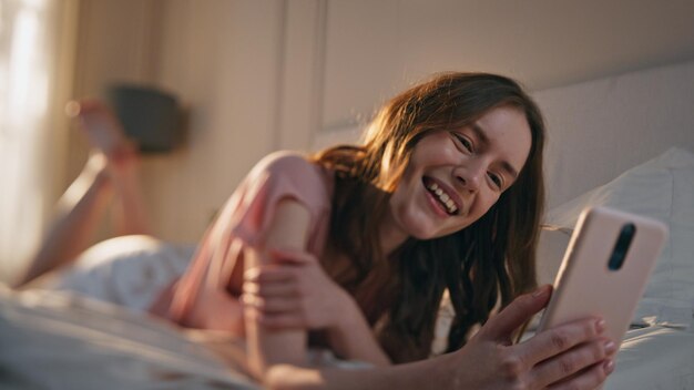 Śmiejąca się kobieta rozmawiająca na konferencji online z bliska zrelaksowana rano dziewczyna leżąca w łóżku