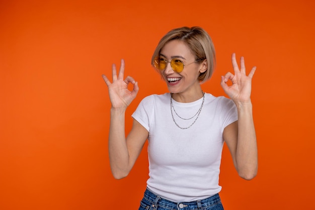 Zdjęcie Śmiejąca się kobieta w białej koszulce pokazująca ok gest izolowany na pomarańczowym tle