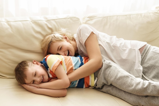 Śmiejąca się mama i syn leżący na kanapie w słoneczny weekendowy dzień