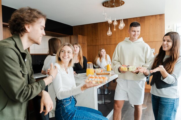 Zdjęcie Śmiejący się przyjaciele świętujący urodziny cieszący się imprezą w domu grupa ludzi młodzi mężczyźni kobiety koledzy jedzący napoje i przekąski przy stole obiadowym